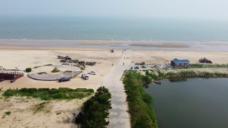 Aerial-cinematic-forward-dolly-view-of-Nanhai-beach-with-boats,-pond-and-people-biking