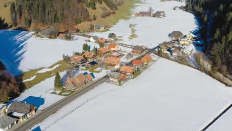 Luftdrohnenaufnahmen-Eines-Kleinen-Dorfes-Im-Emmental-Im-Kanton-Bern,-Schweiz,-Zeigen-Kleine-Stadtgebäude-Und-Heimat-Und-Die-Umliegenden-Schneebedeckten-Berge