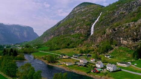 Aerial-drone-forward-moving-shot-of-waterfall-along-mountain-slope-into-Gronsdalslona-river-in-Norway-with-village-houses-in-the-foothills-at-daytime