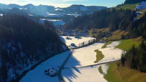 Aerial-drone-footage-of-a-small-village-in-the-emmental-in-the-canton-of-Bern,-Switzerland,-showing-small-town-buildings,-and-home-and-surrounding-snowy-mountains