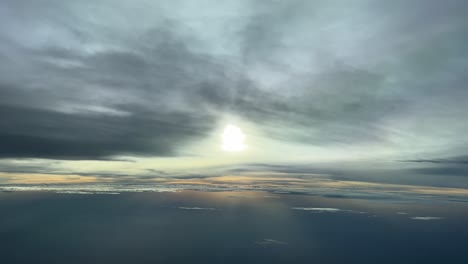 Aerial-view-from-a-jet-cockpit-in-a-cold-winter-afternoon-before-sunset-at-12000-metres-high,-with-the-sun-vealed-behind-some-clouds