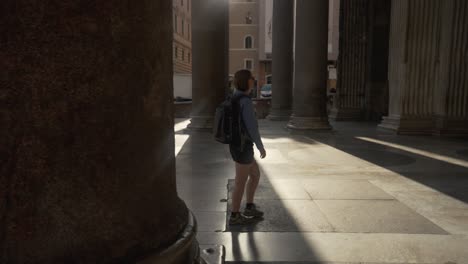 Pan-shot-of-a-woman-walking-between-the-pillars-of-the-Pantheon-with-the-sun-coming-through-in-Rome-in-4k