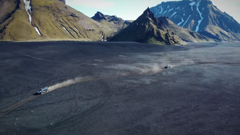Two-Vehicles-Doing-Off-road-In-Wide-Desert-In-Front-Of-High-Mountains-Landscape,-Iceland