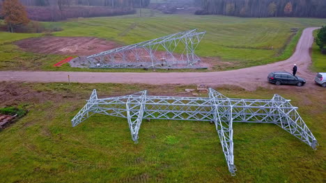 Drone-flying-over-a-high-voltage-tower-on-the-ground-ready-for-lifting-and-installation