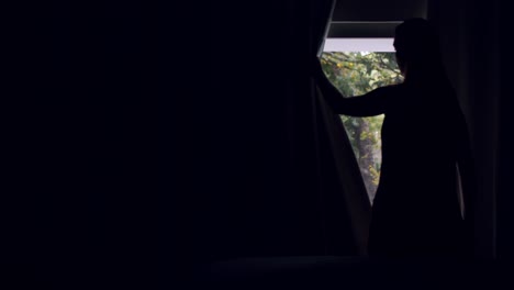 Woman-in-dark-bedroom-opens-the-curtains-and-looks-outside