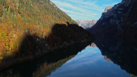 Aerial-Dolly-Over-Calm-Reflective-Lake-In-With-Autumnal-Forest-Trees-On-Valley-Hillside