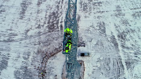 Aerial-view-from-above-of-two-electricians-working-on-a-high-voltage-tower-in-the-snow