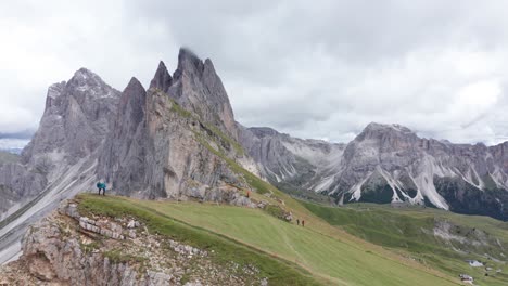 Hikers-on-Seceda-Ridgeline-with-Fermeda-Towers-in-background,-Dolomites,-aerial