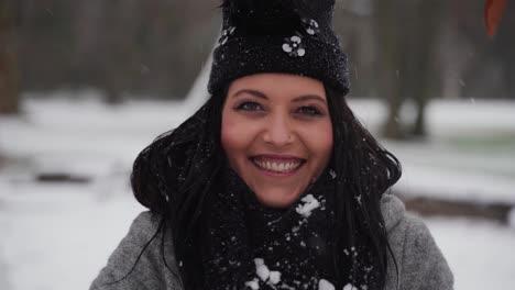 Mujer-En-El-Invierno-En-Un-Parque-Levantando-Las-Manos-Y-Tirando-Nieve-Sobre-Ella-Mientras-Sonríe