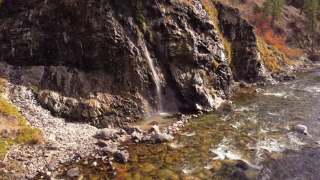 Aerial-drone-shot-flying-in-from-up-river-towards-a-waterfall-hot-spring-in-the-boise-national-forest-Idaho