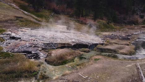 Drone-ellipse-shot-circling-right-of-steam-rising-off-sulfur-natural-hot-spring-in-boise-national-forest-idaho-located-next-to-a-hillside-and-sulfurous-green-creek