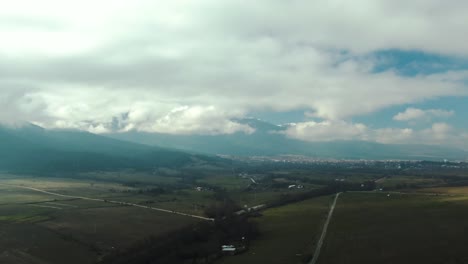 Drone-shot-of-a-field-мountain-and-city-at-the-background-with-cloudy-sky