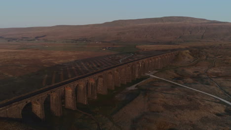 Aerial-Drone-Shot-Pulling-Back-from-Ribblehead-Viaduct-Train-Bridgewith-Long-Shadow-at-Stunning-Sunrise-in-Summer-in-Yorkshire-Dales-England-UK-with-3-Peaks-Whernside-Mountain-in-Background