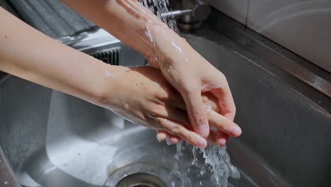 Hände-Der-Frau-Waschen-Ihre-Hände-In-Einem-Waschbecken-Mit-Seifenschaum,-Um-Die-Haut-Zu-Waschen,-Und-Wasser-Fließt-Durch-Die-Hände