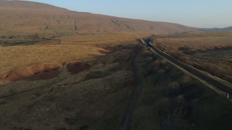 Aerial-Drone-Shot-Following-Train-on-Ribblehead-Viaduct-Train-Bridge-at-Stunning-Sunrise-in-Summer-in-Yorkshire-Dales-England-UK-Panning-to-3-Peaks-Whernside-Mountain