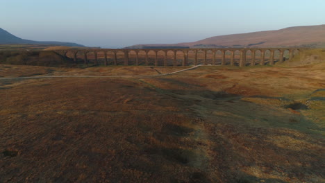 Front-On-Aerial-Drone-Shot-Flying-and-Rising-Towards-and-Over-Ribblehead-Viaduct-Train-Bridge-at-Stunning-Sunrise-in-Summer-in-Yorkshire-Dales-England-UK