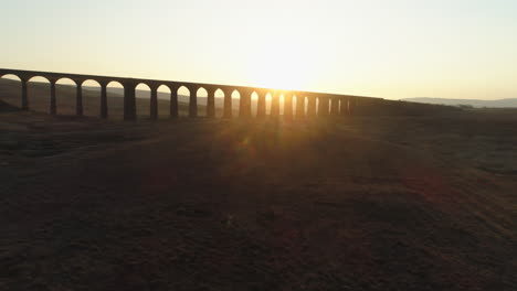 Niedrige-Drohnenaufnahme-Aus-Der-Luft,-Die-Bei-Atemberaubendem-Sonnenaufgang-Im-Sommer-In-Den-Yorkshire-Dales,-England,-Großbritannien,-In-Richtung-Der-Silhouette-Der-Ribblehead-Viadukt-Zugbrücke-Aufsteigt