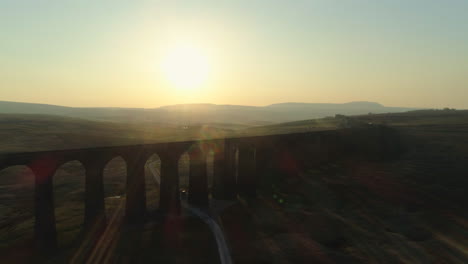 Drohnenaufnahme-Aus-Der-Luft,-Die-Sich-über-Der-Silhouettierten-Ribblehead-Viadukt-Zugbrücke-Bei-Atemberaubendem-Sonnenaufgang-Im-Sommer-In-Yorkshire-Dales,-England,-Großbritannien,-Mit-Hügeln-Im-Hintergrund-Erhebt