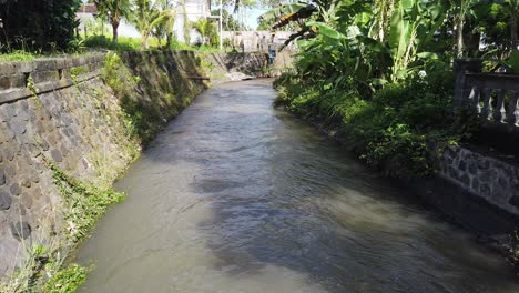 Balinese-River-Path-South-East-Asia,-Brown-Water-Channel-Gianyar-Bali,-Indonesia-Daytime-Landscape-with-Banana-Trees,-Wind-Blowing,-Clear-Light