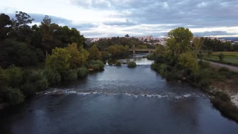 Drone-flying-over-river-during-sunset-near-forrest