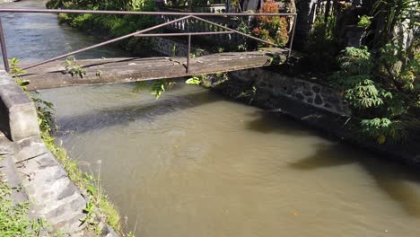 Establishing-Shot-Brown-Dirty-Water-River,-Rainy-Season,-Bali-Indonesia-Daylight-Lonely-Wooden-Bridge
