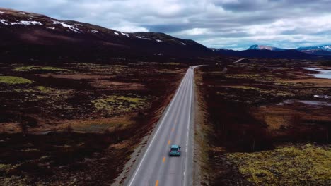 Drone-shot-of-car-driving-on-an-empty-road-in-Iceland-between-the-hills-and-snow
