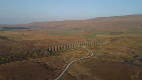 Aerial-Drone-Shot-Rotating-showing-Ribblehead-Viaduct-Train-Bridge-from-far-away-at-Stunning-Sunrise-in-Summer-in-Yorkshire-Dales-England-UK-with-3-Peaks-Whernside-Mountain-in-background