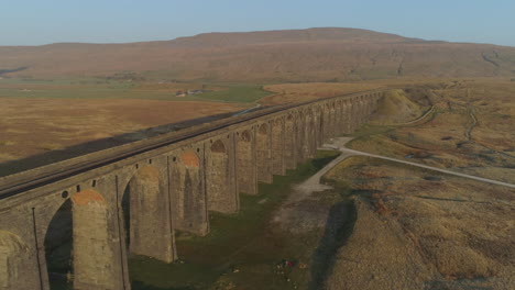 Aerial-Drone-Shot-Along-Ribblehead-Viaduct-Train-Bridge-at-Stunning-Sunrise-with-long-shadows-in-Summer-in-Yorkshire-Dales-England-UK-with-3-Peaks-Whernside-Mountain-in-Background