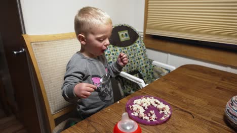 Wide-handheld-shot-of-kid-eating-rice-and-meat-with-a-metal-spoon-sitting-at-the-kitchen-table