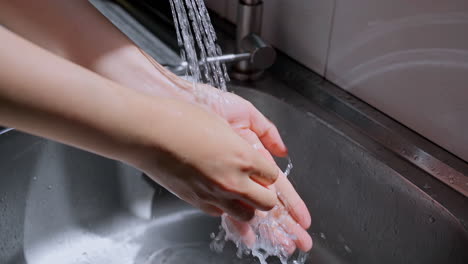 Hände-Der-Frau-Waschen-Ihre-Hände-In-Einem-Waschbecken-Mit-Schaum,-Um-Die-Haut-Zu-Waschen,-Und-Wasser-Fließt-Durch-Die-Hände