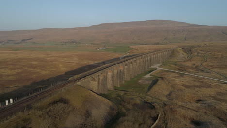 Aerial-Drone-Shot-Pulling-away-from-Ribblehead-Viaduct-Train-Bridge-at-Stunning-Sunrise-in-Summer-in-Yorkshire-Dales-England-UK-with-3-peaks-Whernside-mountain-in-background