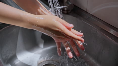 Hände-Der-Frau-Waschen-Ihre-Hände-In-Einem-Waschbecken-Mit-Seife,-Um-Die-Haut-Zu-Waschen,-Und-Wasser-Fließt-Durch-Die-Hände