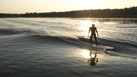 Surfer-Auf-Longboard-Surfwelle-Hinter-Boot-Mit-Kreuzschritt-Im-Sonnenuntergang