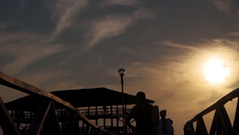 A-male-surfer-chases-down-friends-on-the-pier-at-sunset,-slow-motion-tracking-shot