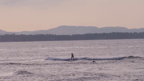 Surfer-in-silhouette-riding-wave-with-mountains-in-background