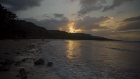 Gleiten-Sie-Einen-Strand-Hinunter-In-Richtung-Eines-Wunderschönen-Sonnenuntergangs,-Während-Die-Wellen-In-Zeitlupe-Auf-Den-Strand-Schlagen