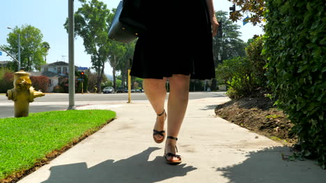 Upward-pan-of-woman-walking-down-a-sidewalk-in-Los-Angeles