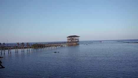 Three-surfers-retreat-from-surfing-area-at-the-end-of-a-long-pier-with-a-multi-level-observation-tower