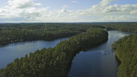 Aerial-footage-of-a-Finnish-lake-in-summer,-blue-sky,-heavy-clouds-and-sun,-long-island