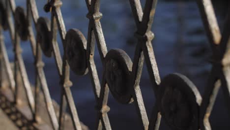 Metal-old-fence-by-the-river-with-x-shape-ornament-and-moody-sharp-contrast,-deep-blue-water-in-the-background
