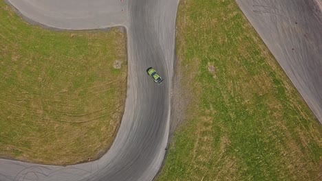 Aerial-shot-of-a-car-drifring-on-high-speed-on-a-turn,-green-grass-and-a-race-track,-top-view-shot