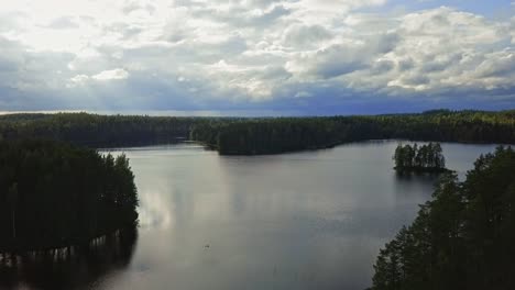 Aerial-footage-of-a-Finnish-lake-in-summer,-blue-sky,-heavy-clouds-and-sun