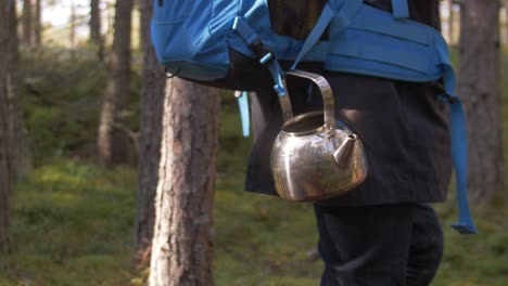 Metal-shiny-tea-pot-with-reflection-of-the-forest-and-autumn-slow-motion-atmosphere,-blue-tourist-bag