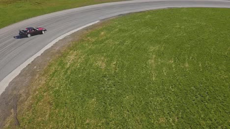 Aerial-shot-of-a-green-car-drifring-on-high-speed-on-a-turn,-green-grass-and-a-race-track,-top-side-tracking-shot