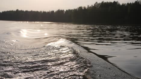 Big-wave-on-a-lake-while-in-a-boat-with-sun-shining-in-the-background-blurry-forest-moody-evening-atmoshere