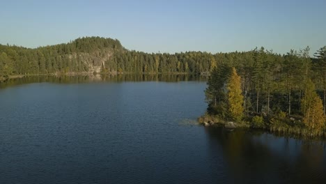 Finnish-lake-with-beautiful-island-and-rocky-shore,-autumn-trees-and-deep-blue-water