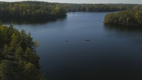 Epische-Aufnahme-Eines-Nordischen-Waldes-In-Finnland,-Mann-Beim-Kajakfahren-In-Einem-See,-Rote-Und-Gelbe-Boote,-Nationalpark-Mit-Inseln-Und-Wald,-Steinufer-Und-Tiefblaues-Wasser