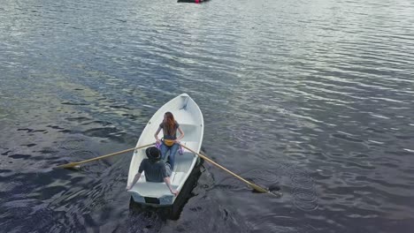 Feminist-free-woman-on-a-boat-with-paddle-and-relaxing-man-in-a-hat,-aerial-drone-shot