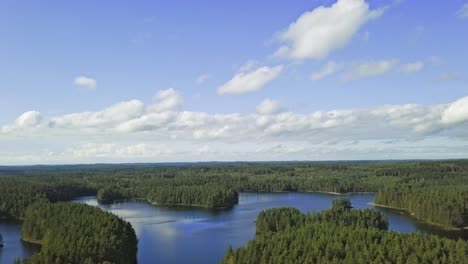 Aerial-footage-of-a-Finnish-lake-in-summer,-blue-sky,-heavy-clouds-and-sun,-revealing-shot-from-top-to-bottom,-carelia