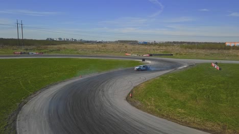 Aerial-shot-of-a-car-drifring-on-high-speed-on-a-turn,-green-grass-and-a-race-track,-top-side-shot